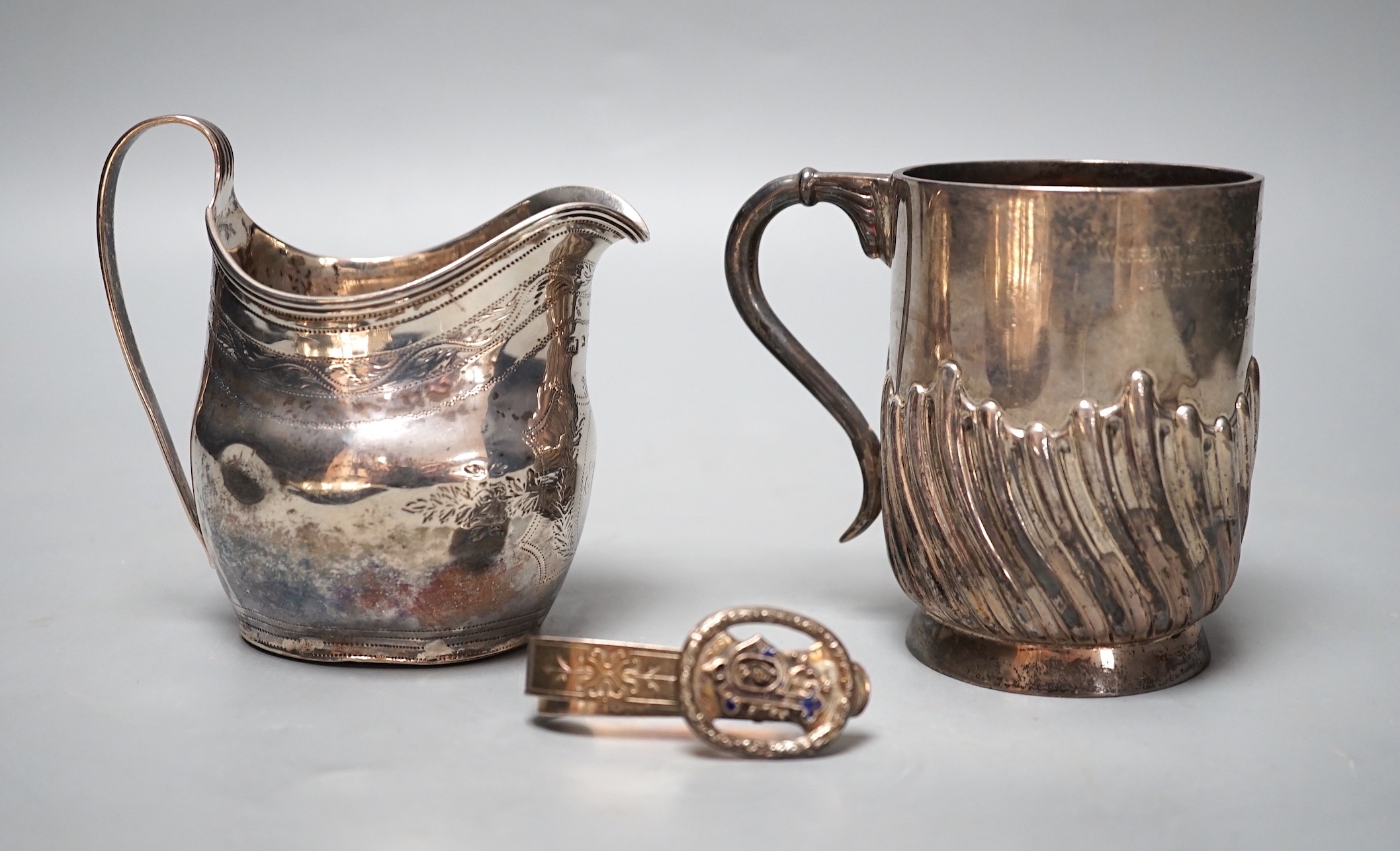 A George III silver cream jug, London, 1800, a later silver mug and a white metal and enamelled initiallled clip?, gross 8.5oz.